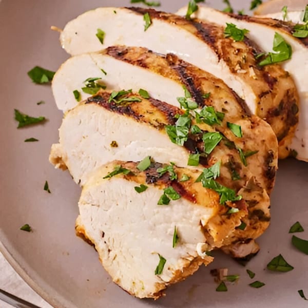 Sliced grilled chicken breast, garnished with fresh parsley, on a gray plate.