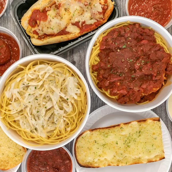 An overhead view of By the Bucket Mesa's Italian dishes, including spaghetti with red sauce, alfredo, and garlic bread.