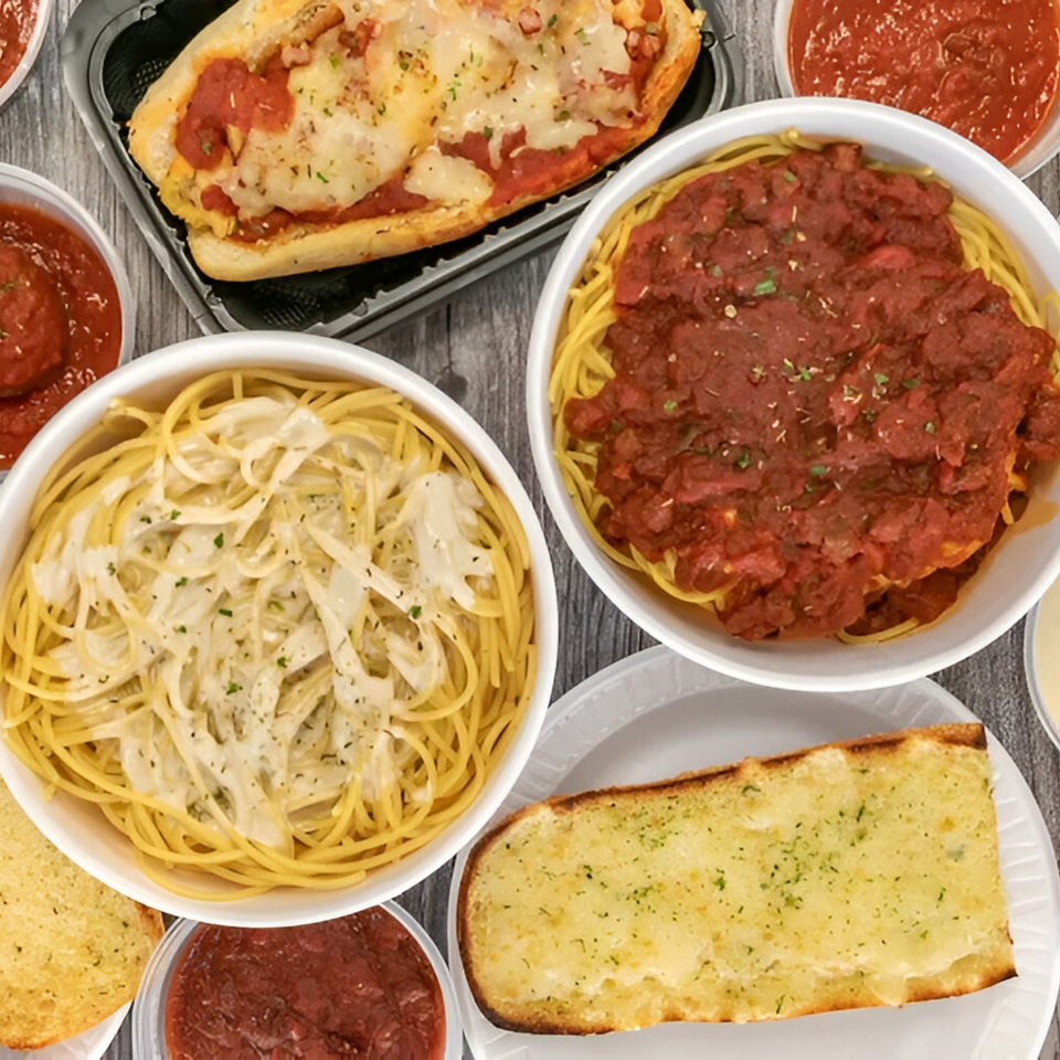 An overhead view of By the Bucket Mesa's Italian dishes, including spaghetti with red sauce, alfredo, and garlic bread.