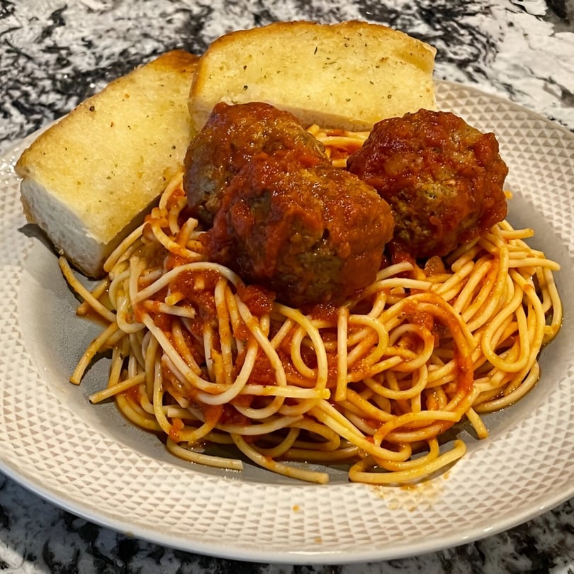Spaghetti with meatballs and garlic bread on a white plate from By the Bucket Mesa.